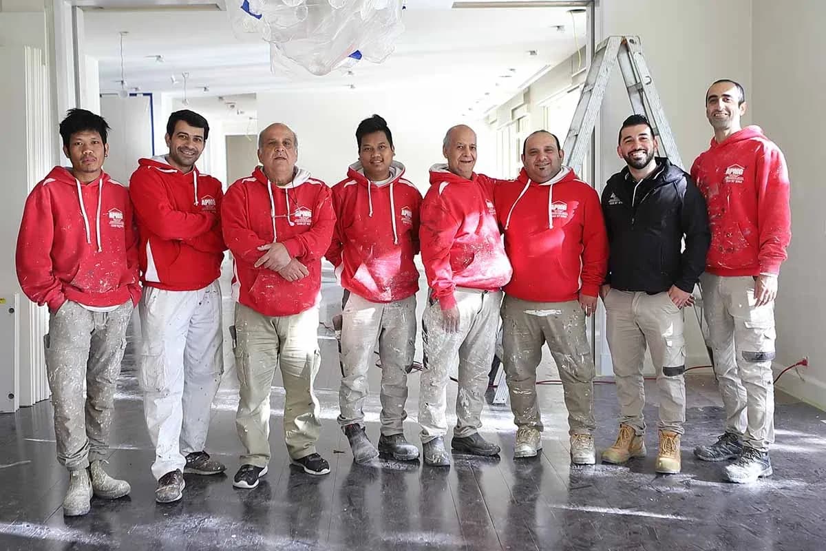 Members of the painting crew standing together on a commercial interior job, a stepladder behind them